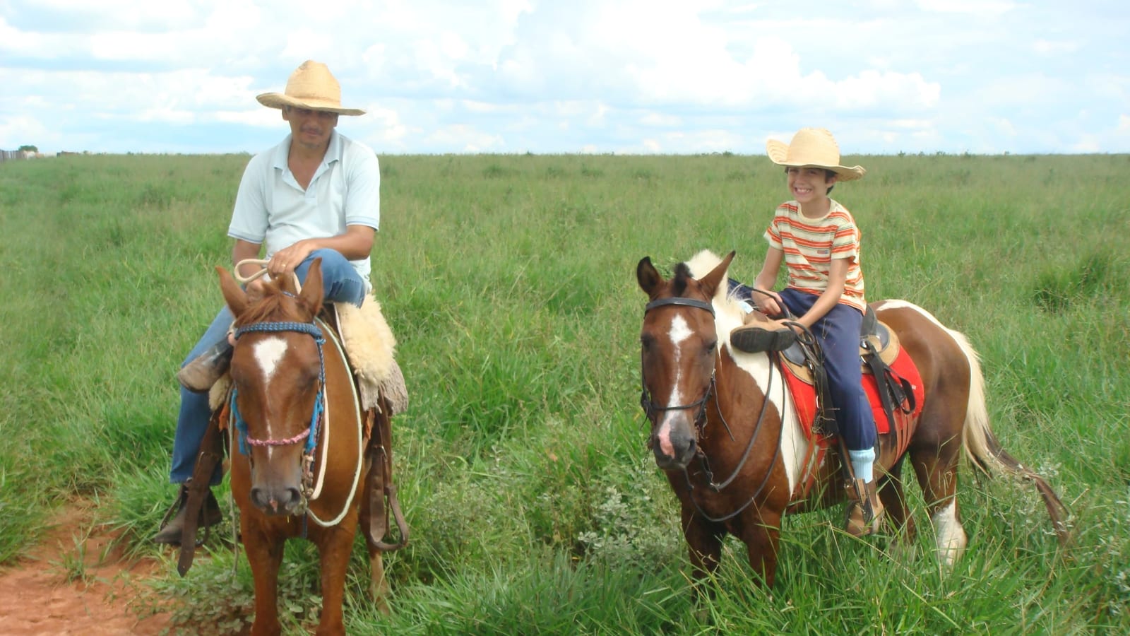 Pedro criança e o pai, cada um a cavalo, no pasto da fazenda